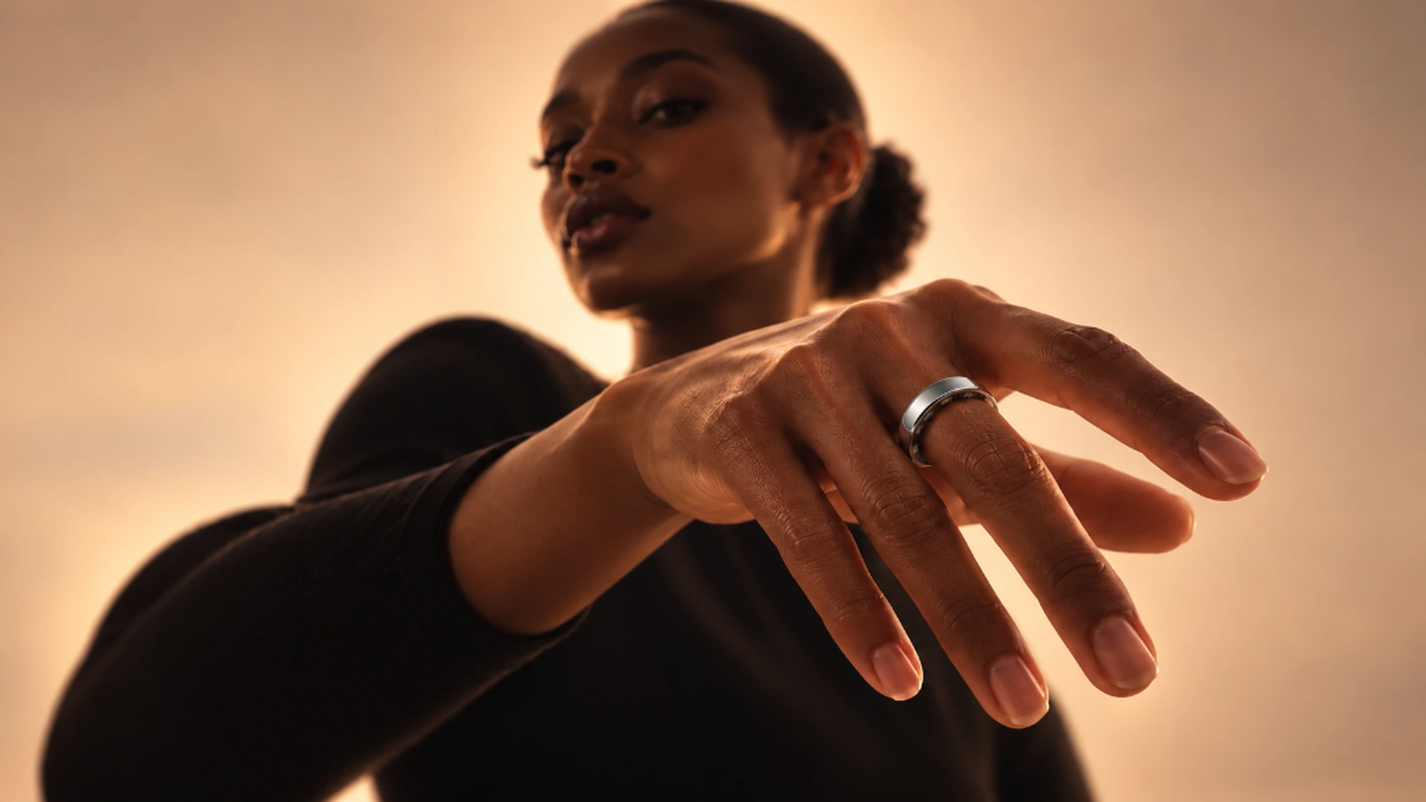 A model extending her hand toward the camera, with a polished silver ring in focus against warm amber light